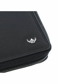 Gros plan sur un coin de portefeuille noir zippé avec des bords cousus et un petit emblème de logo argenté à cornes.