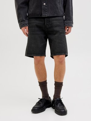 Zwarte denimshorts met een ontspannen pasvorm, met een rechte pijp en een rafelrand. Gepaarde met donkerbruine geribbelde sokken en zwarte veterschoenen.