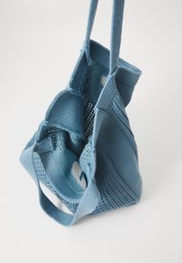 Blauwe, gebreide stoffen tas met dubbele handvatten en een open bovenkant, met een gestructureerde weving en een ronde vorm voor flexibele draagmogelijkheden.