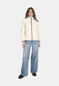 Giacca zip con cappuccio di un beige chiaro, con polsini elasticizzati e tasche laterali, abbinata a jeans in denim blu a gamba larga e scarpe nere.