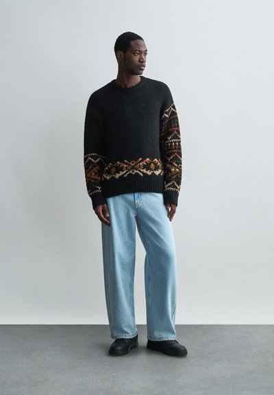 Fekete kötött pulóver, narancssárga, barna és krém színű mintás vállrésszel, világoskék bővített szárú farmernadrággal és fekete cipővel párosítva.