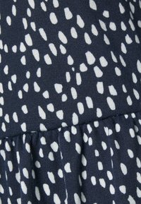 Tecido azul-marinho com um padrão branco salpicado; apresenta uma renda franzida na bainha, criando textura e dimensão no design.