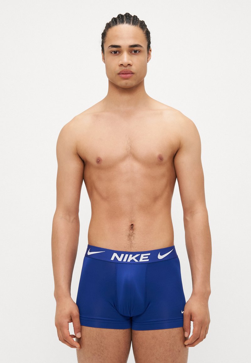Boxeri Nike albaștri cu logo pe talie albă, fabrică netedă, design ajustat și croială de înălțime medie, prezentate pe un model masculin fără cămașă.