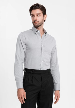 Camisa abotonada de color gris claro con mangas largas, hecha de tela suave, combinada con pantalones negros que incluyen un cinturón y un frente plisado.