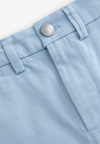 Pantaloni in tessuto azzurro chiaro con una texture liscia, dotati di un dettaglio in bottone argentato etichettato "BAKER" e una cintura cucita in modo ordinato.