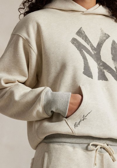 Ανοιχτό κρεμ χρώμα φούτερ με φθαρμένο γκρι λογότυπο NY, κα kangaroo τσέπη, ριμπ μανσέτες σε αντίθετο γκρι τόνο και υπογραφή στη βάση.