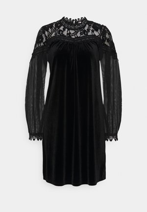 Zwarte fluwelen jurk met een kanten inzetstuk, lange doorzichtige mouwen en een gegolfde kanten rand bij de halslijn en mouwboorden.