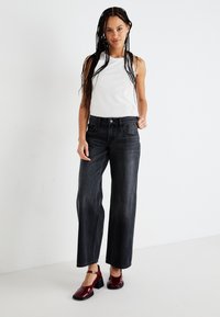 Jeans de pierna ancha negros con cintura alta, combinados con una camiseta ajustada blanca y zapatos de tacón burdeos. Diseño sencillo y recto con bolsillos.