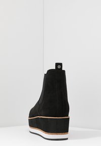 Svart nubuck plattform ankelboot med elastisk sidopanel och dragflik, med ett lagrat sula i svart, kork och vitt.