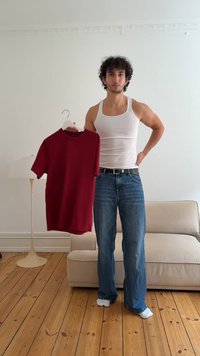 T-shirt rosso a maniche corte appeso a una gruccia, con scollo rotondo, texture liscia e retro leggermente più lungo. Modello in canotta bianca e jeans.