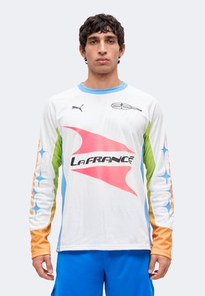 Jeune homme portant un maillot de sport à manches longues en mesh blanc avec des manches multicolores et le texte "La France", assorti à un short bleu vif.