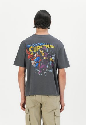 Grijze katoenen t-shirt met een kleurrijke stripachtige afbeelding op de achterkant met "Superman" en actiefiguren. Korte mouwen, losse pasvorm.