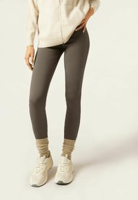 Leggings gris en tissu extensible, style ajusté, associés à un pull beige et des baskets beiges. Les poignets ont une texture côtelée.