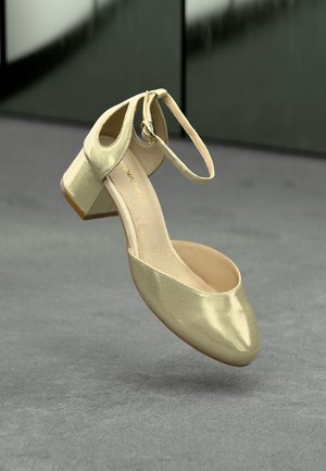 Chaussure à talon dorée en métal avec un bout ouvert et une bride de cheville. Possède une forme arrondie, une texture lisse et un talon bloc bas.