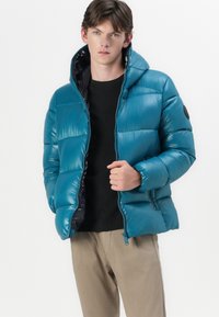 Teal puffer jacket with a high collar, glossy finish, and dark inner lining. Features a front zipper and ribbed wrist cuffs.