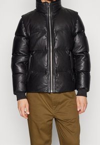 Svart läderpuff-jacka med hög krage, blixtlås framtill och ribbade manschetter. Har vadderade sektioner och sidofickor.