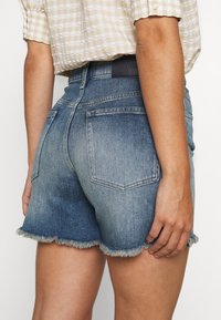 Shorts de denim con un dobladillo desflecado, que presentan un lavado en degradado de azul oscuro a claro, dos bolsillos traseros y una cintura suave.