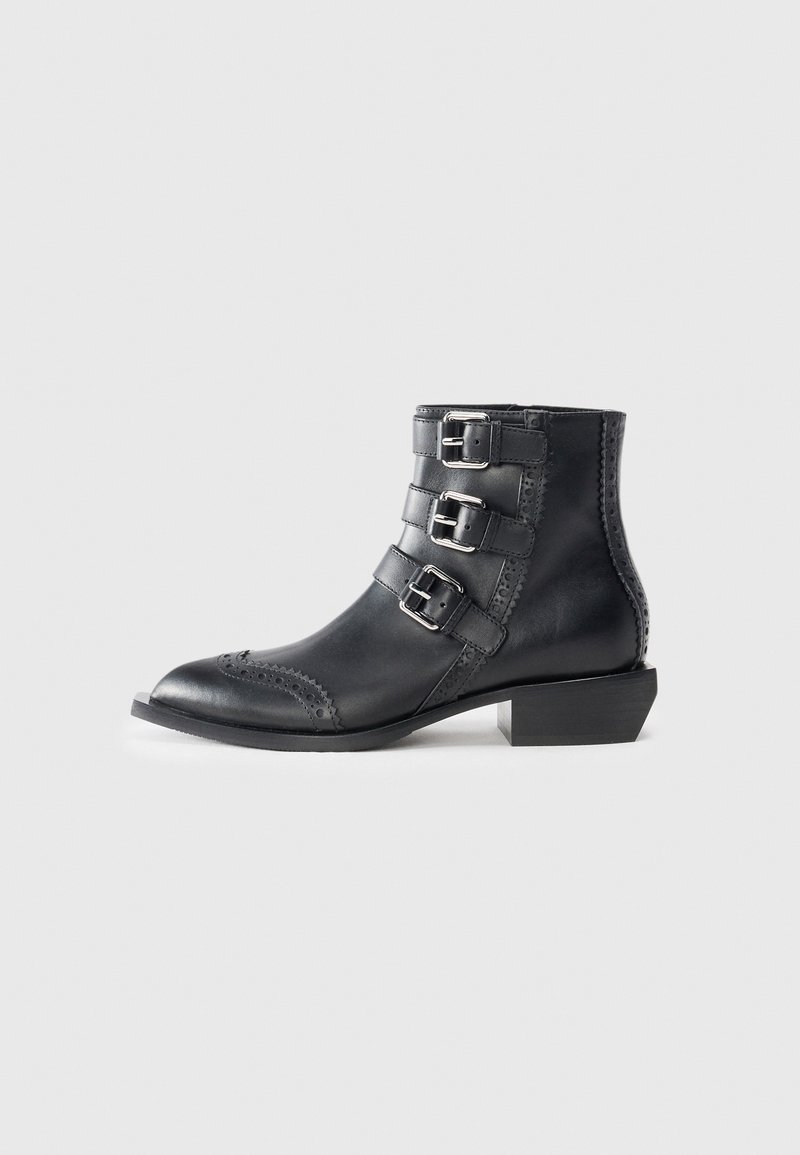 Stivaletti neri in pelle con tre fibbie argentate, dettagli decorativi brogue intorno alla punta e tacco basso a blocco.