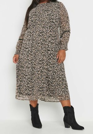 Kvinde iført en langærmet, midi-kjole med leopardprint og elastiske manchetter, kombineret med sorte ankelstøvler med blokhæl.