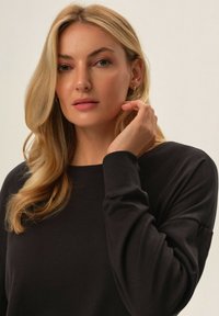 Czarna bluza z długim rękawem, miękka w dotyku, okrągły dekolt i luźny krój. Modelka ma falujące blond włosy i neutralny wyraz twarzy.