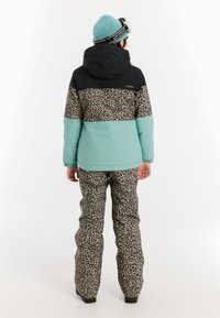Abbigliamento da sci invernale composto da una giacca nera, verde menta e con stampa leopardata, abbinata a pantaloni in stampa leopardata; il materiale sembra isolato.