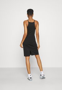 Schwarzes, enges Kleid mit dünnen Trägern, Mid-Thigh-Länge, mit einem Schlitz im Rücken. Getragen mit weißen Socken und schwarz-weißen Sportschuhen.