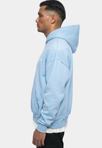 Helle blaue Pullover-Hoodie mit Kängurutasche, gerippten Bündchen und einer großen Kapuze. Mit minimalistischem Text auf der Vorderseite. Hergestellt aus weichem Material.