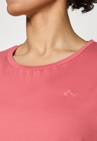 Pink fabric T-shirt with a round neckline, featuring smooth texture and a subtle dot pattern on the chest area.