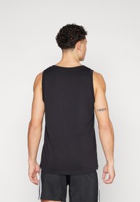 Top de tanque preto sem mangas feito de um tecido macio, com decote redondo e um corte solto. Inclui uma tatuagem visível no braço da pessoa que veste.