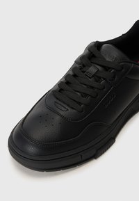 Fekete bőr sneaker texturált felülettel, lapos fűzőkkel és perforált orr résszel. Gumi talppal és hitelesített logóval rendelkezik a nyelvén.