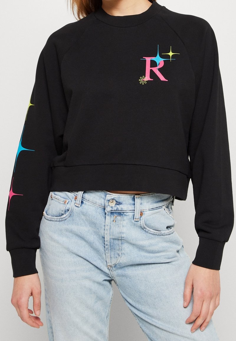 Sweatshirt corto nero con orlo a coste, maniche lunghe a raglan e grafica scintillante multicolore. Tessuto morbido con una vestibilità rilassata.