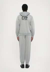 Grå sweatshirt og bukser sæt lavet af glat stof, med hætte, elastiske manchetter og et sort EA7-logo på ryggen.