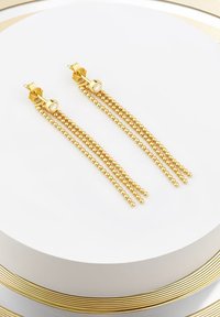 Guldtonade örhängen med tre strängar av små pärlor, med en cirkulär studs och en framträdande klar ädelsten som accent ovanpå.