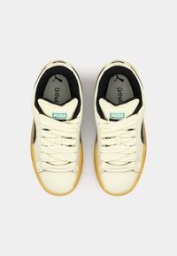 Cream-colored sneakers with black accents, textured laces, orange rubber soles, and green label detail featuring the Puma logo.