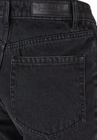 Poche arrière et ceinture d'un jean en denim noir avec une étiquette en cuir indiquant la marque "Urban Classics Denim Factory".
