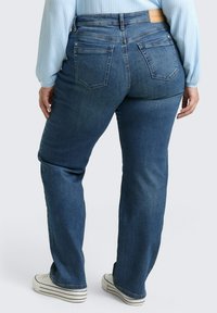 Ciemnoniebieskie dżinsy z wysokim stanem, prostymi nogawkami, pięcioma kieszeniami i brązową skórzaną metką z tyłu w pasie. Casualowy wygląd z trampkami.