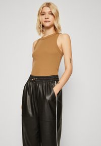 Top marrón sin mangas con textura acanalada combinado con joggers de cuero negro que cuentan con cintura ajustable y detalles de raya blanca a los lados.