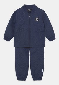 Mörkblå kviltad jacka och byxset med ribbad krage, dragkedjestängning och förstärkt sömnad. Har en strukturerad bikake-mönster.