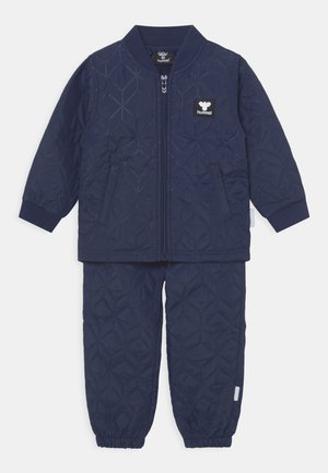 Granatowy zestaw kurtki pikowanej i spodni z prążkowanym kołnierzem, z zamkiem błyskawicznym i wzmocnionymi szwami. Posiada teksturowany wzór w plaster miodu.