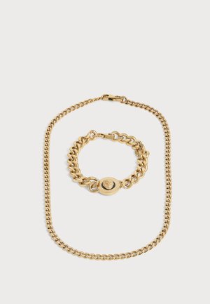 Collar de cadena dorada y pulsera a juego con medallón ovalado que presenta un diseño de cabeza de león sobre un fondo blanco liso.