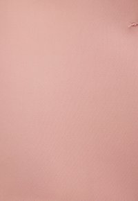 Lichtroze stof met een kleine scheur en rafelige rand nabij de rechterbovenhoek.