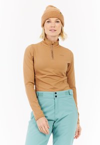 Bruine langesleeve basislaag met een ritskraag en logo; gecombineerd met lichtteal broek met twee zwarte knopen en tabdetails.