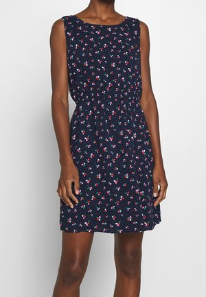 Vestido sin mangas azul marino con patrón floral pequeño y colorido y cintura fruncida, llevado por una persona con tono de piel oscuro.