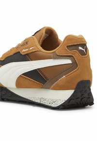 Sneaker in suede marrone con accenti neri e bianchi, dotata di una suola in gomma nera testurizzata e loghi Puma sui lati e sul tallone.