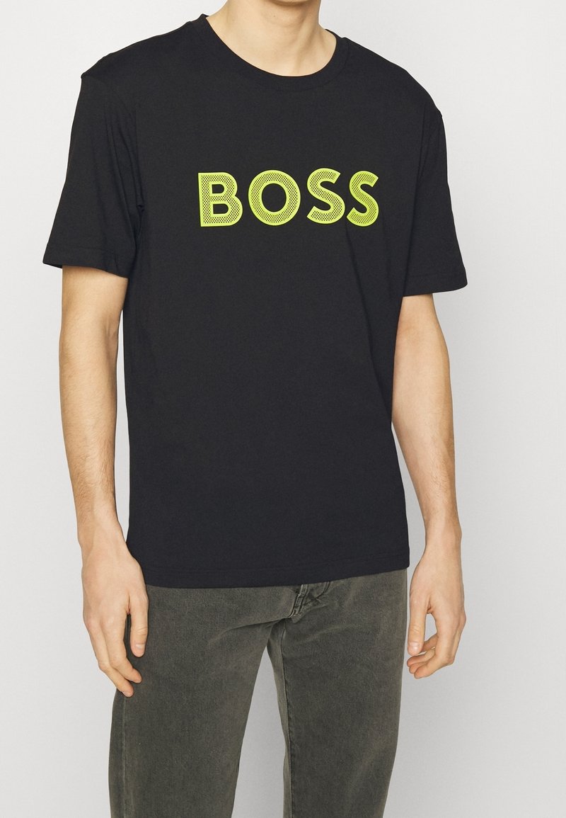 T-shirt en coton noir à manches courtes, affichant un grand logo "BOSS" vert en lettres sobres sur la poitrine. Texture lisse et coupe classique.