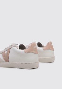 Zapatillas blancas y beige con un logo V texturizado, acentos de ante suave y un acabado de cuero liso. Presentan una lengüeta trasera contrastante.