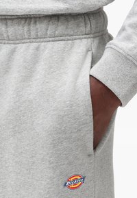 Gray cotton sweatpants with an elastic waistband, side pocket openings, and a colorful Dickies logo patch near the pocket.