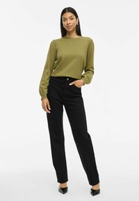 Olijfgroene langharige trui met puffed sleeves, gecombineerd met hoge taille zwarte rechte jeans en zwarte puntige hakken.
