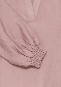 Staubrosa Bluse mit V-Ausschnitt und gerafften Puffärmeln. Der strukturierte Stoff weist subtile Rippungen auf, mit elastischen Bündchen für einen taillierten Look.