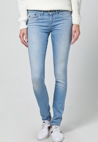 Light blue denim skinny jeans with a faded texture, five-pocket design, and a mid-rise waist, paired with white sneakers and a knit sweater.
